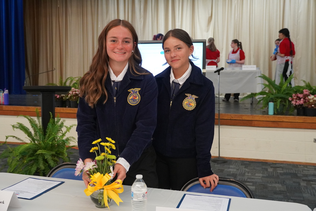 Two high school FFA students are standing behind a table working on a small flower arrangement.