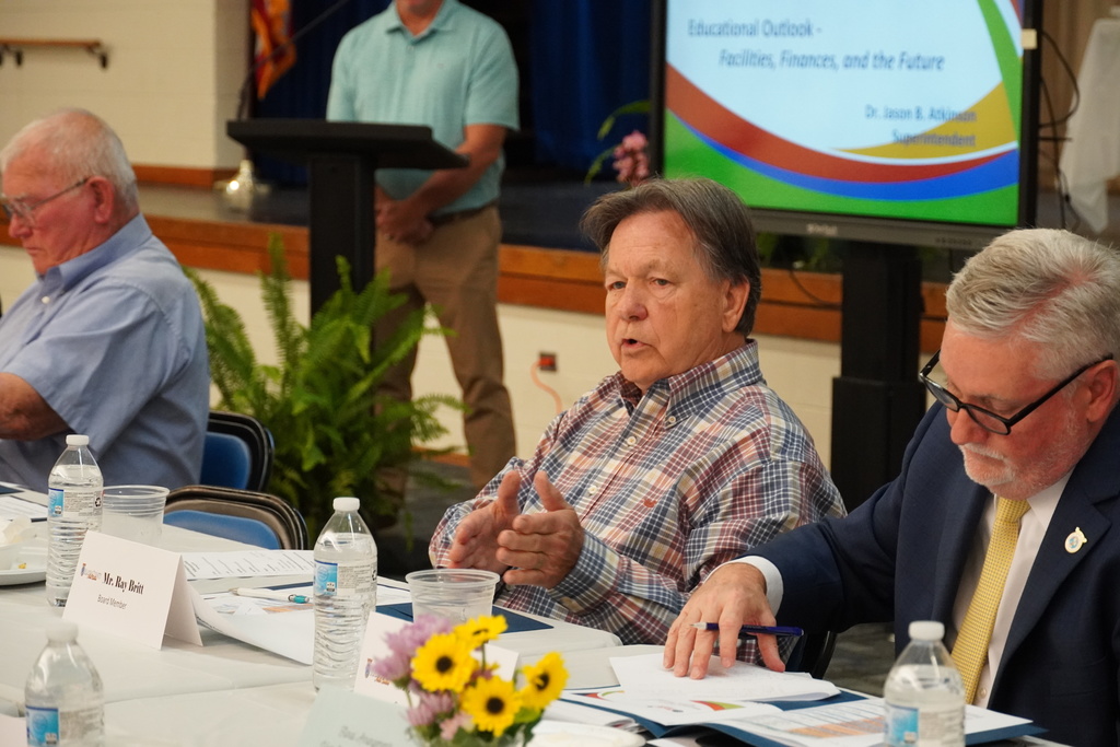 An man in a plaid shirt is asking a question during a meeting.