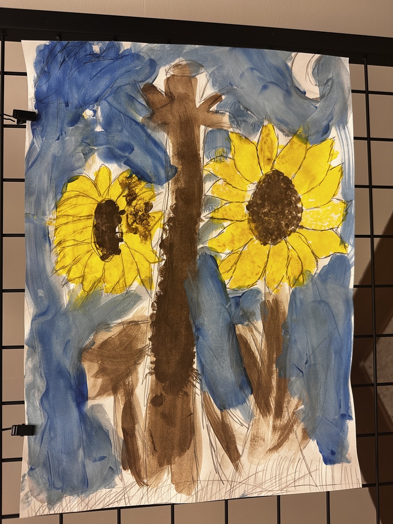 Colorful painting featuring two bright yellow sunflowers with dark brown centers set against an abstract background of blue and brown brushstrokes, with visible white paper showing through on the left side.