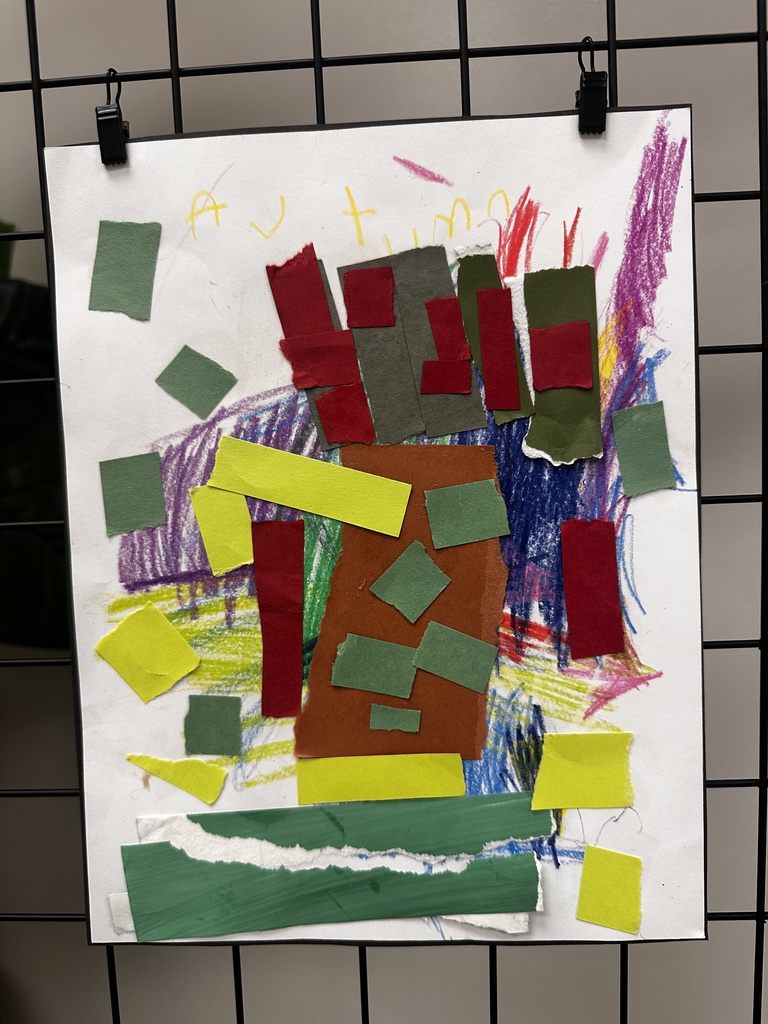 Child's abstract mixed-media collage and drawing titled "Autumn" featuring colorful crayon scribbles in purple, blue, green, yellow, red, and pink with glued-on colored paper rectangles and squares in dark red, dark green, and yellow with torn edges, and a prominent brown irregular paper shape in the center with a dark green paper strip at the bottom.