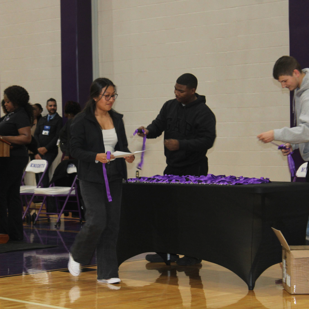 A young woman in a black blazer accepts her award and receives a purple lanyard 