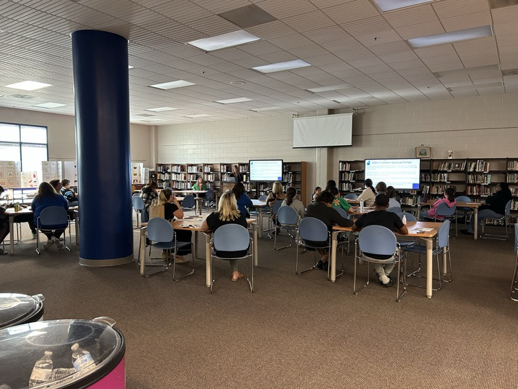 several people sitting at tables in a library looking at two screens while a woman presents information