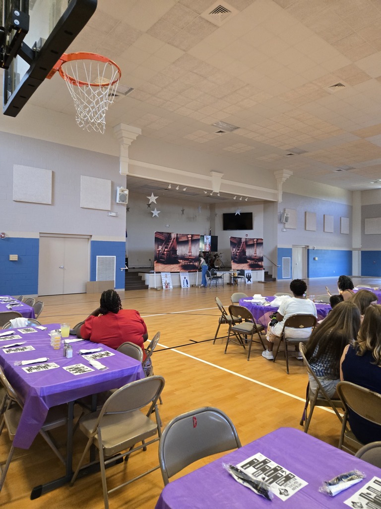 Spectators sitting at long tables decorated with purple linens, enjoying a meal and socializing during the Beta Club Showcase.