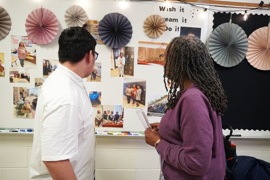 A student is talking with an adult and pointing out various photos that are displayed on a white board.