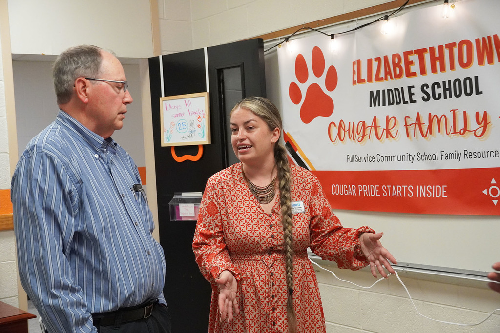 Two adults talk togehter in front of a banner that says Elizabethtown Middle School Cougar Family.