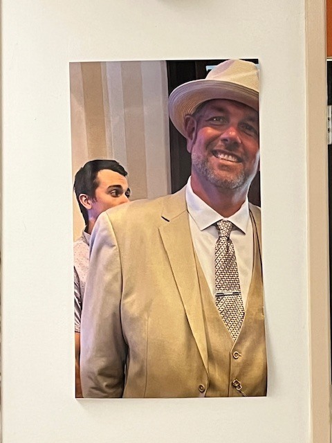 Portrait of a smiling man in a tan suit and hat displayed on a wall.