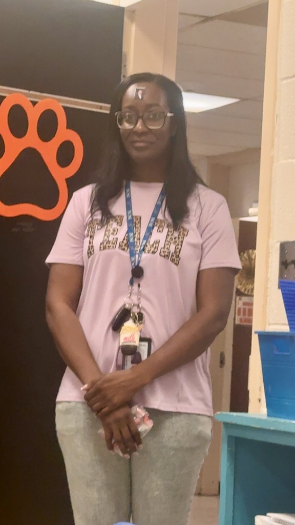 Staff member wearing a purple shirt and ID lanyard standing near a doorway with a cougar paw print sign.