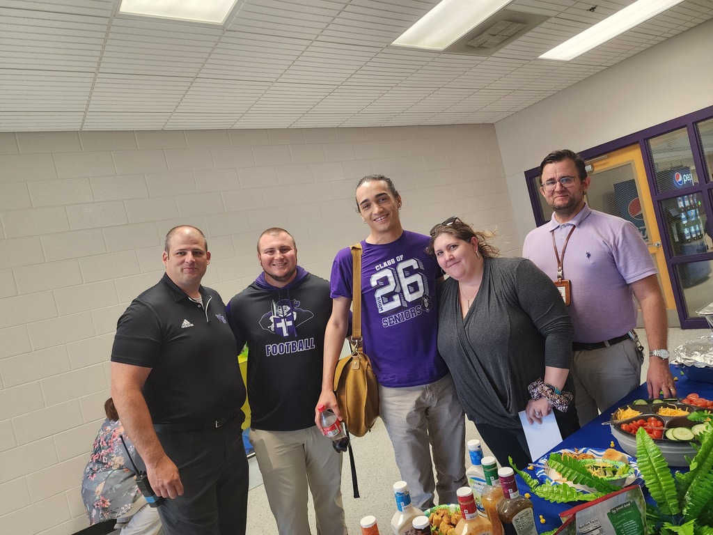 Five staff members smiling and posing in a school lobby