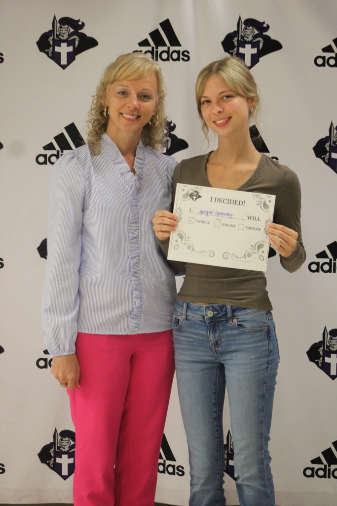 A student and an adult stand in front of a school-branded backdrop, smiling at the camera. The student holds a certificate that reads “I Decided!” with a box checked for enrolling, celebrating their post-graduation plans.