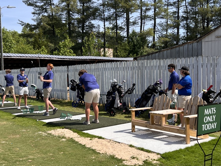 three students on cement pads practicing their golf swings