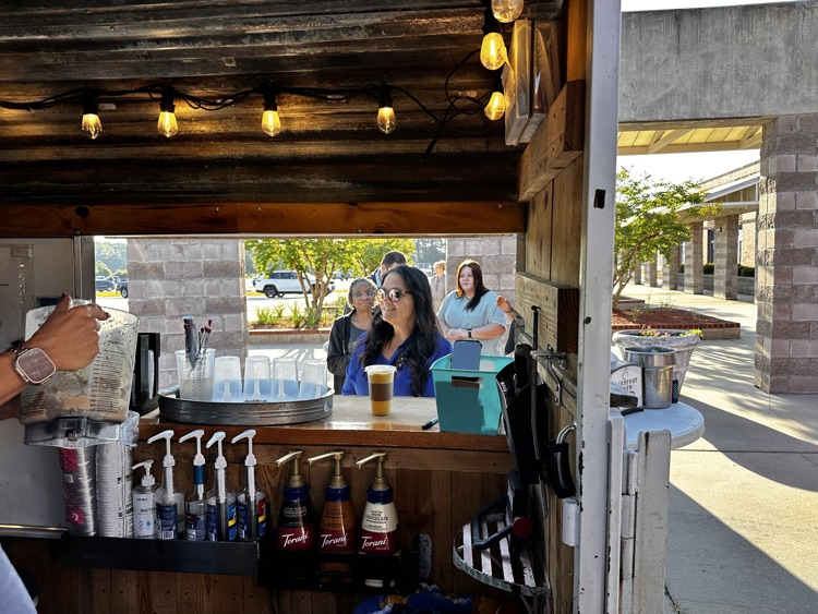 Inside of a coffee cart with a woman smiling ordering at the counter.