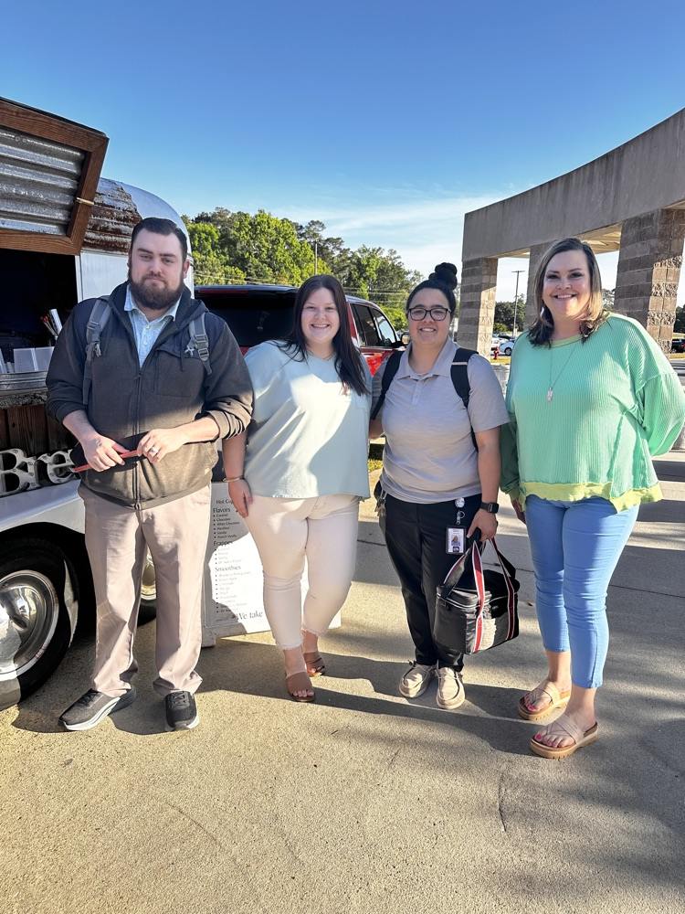 A group of staff members stand together outside, next to a coffee cart.