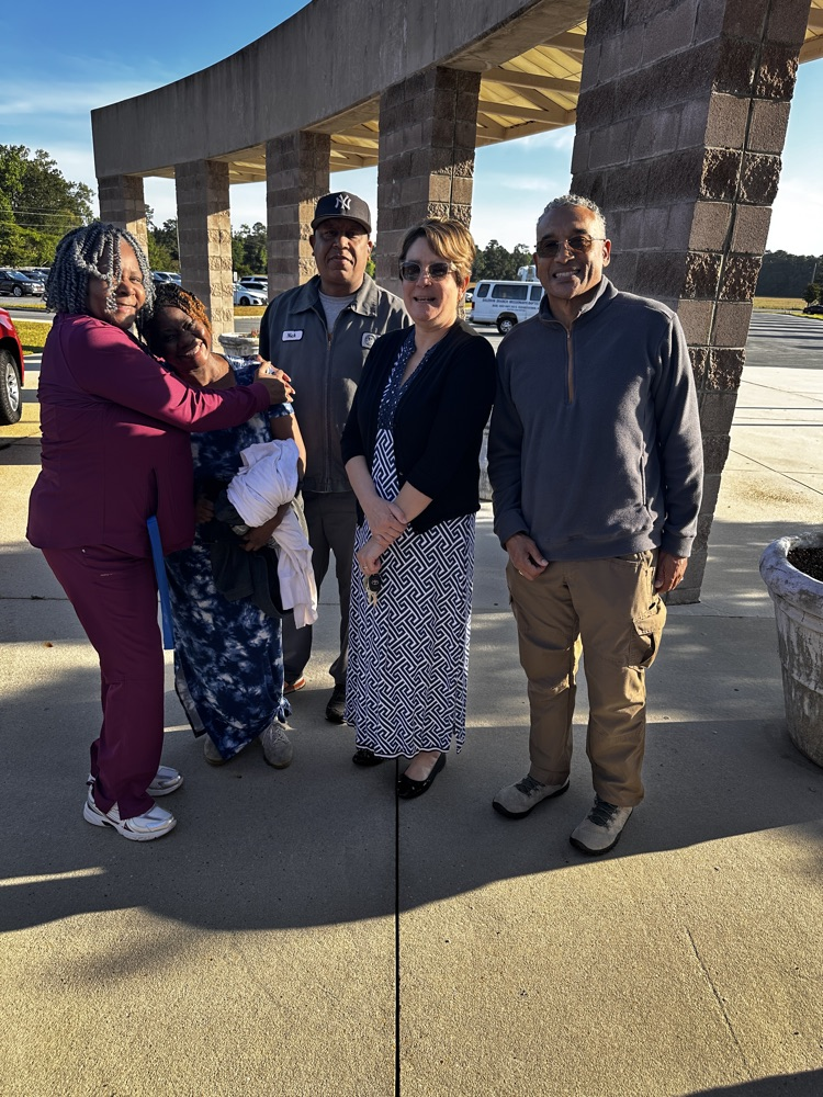 A group of staff members stand together smiling outside.