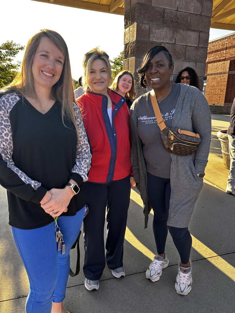 A group of staff members stand together smiling outside waiting in line.