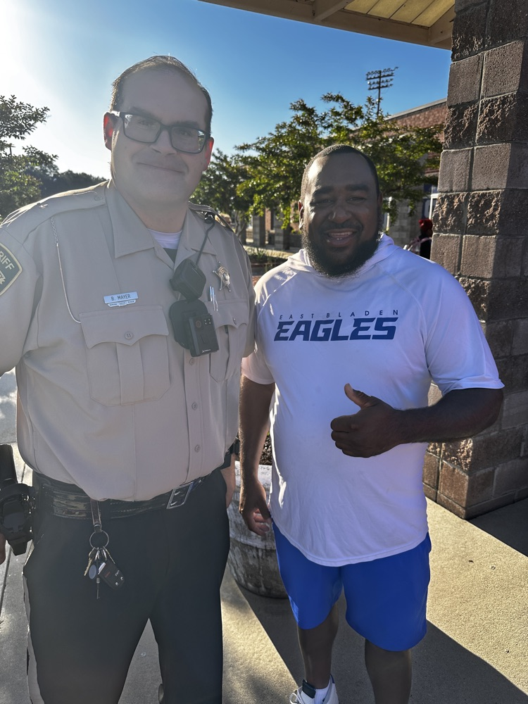 A SRO and school coach stand together smiling outside.