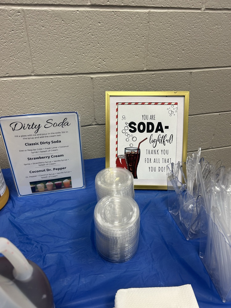 Table with blue table cloth, gallons of syrups and soads, and menus for a dirty soda bar