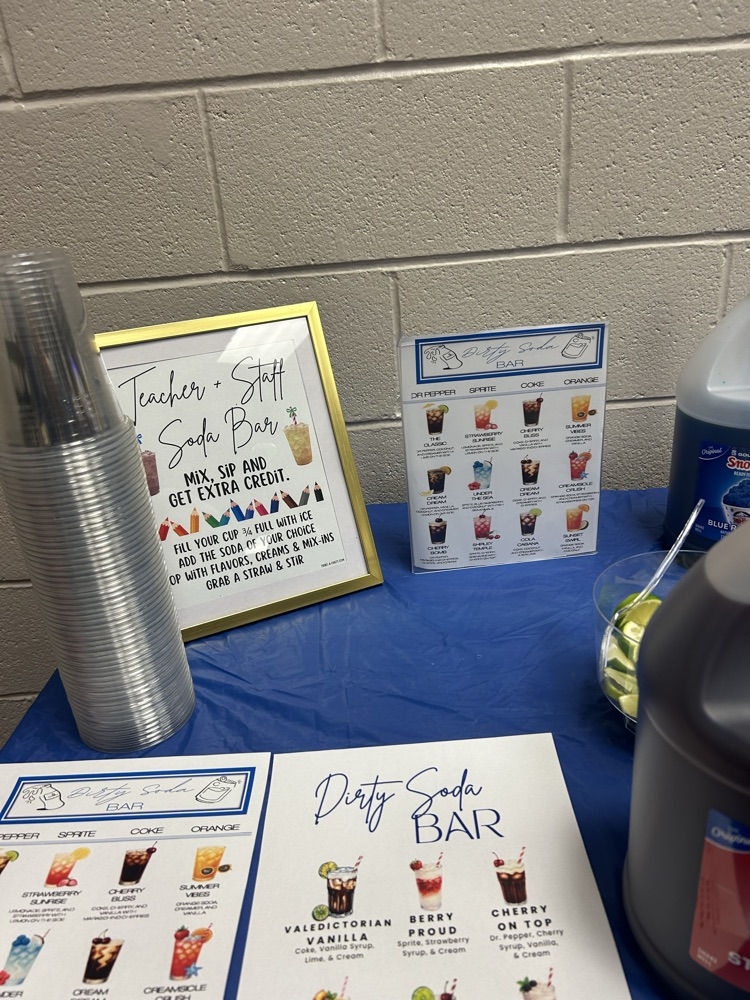 Table with blue table cloth, gallons of syrups and soads, and menus for a dirty soda bar