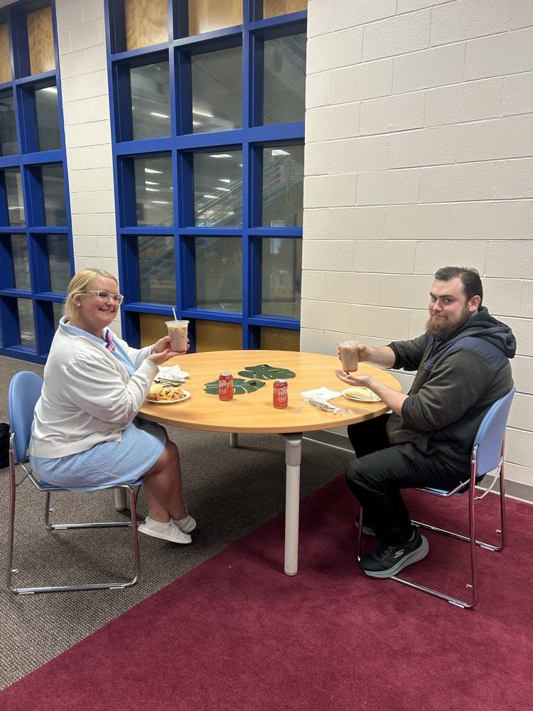 teacher in a blue dress and white cardigan and a teacher in a black pants and black jacket holding a cup of dirty soda