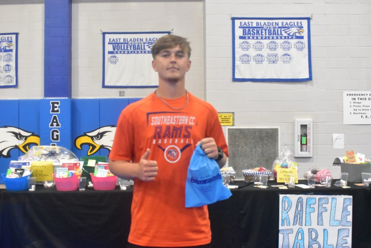 young man in orange shirt posing with a raffle prize he won from Leinwands