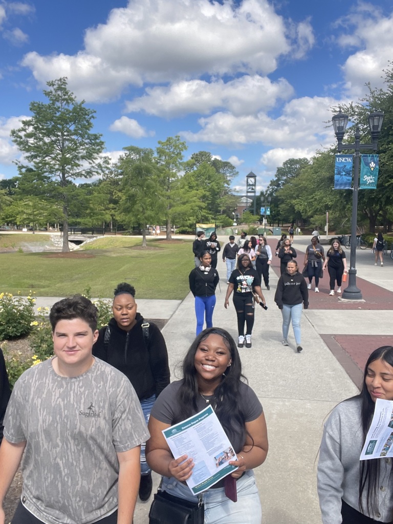 Students walking around UNCW campus. There is green grass, blue sky, and clouds.