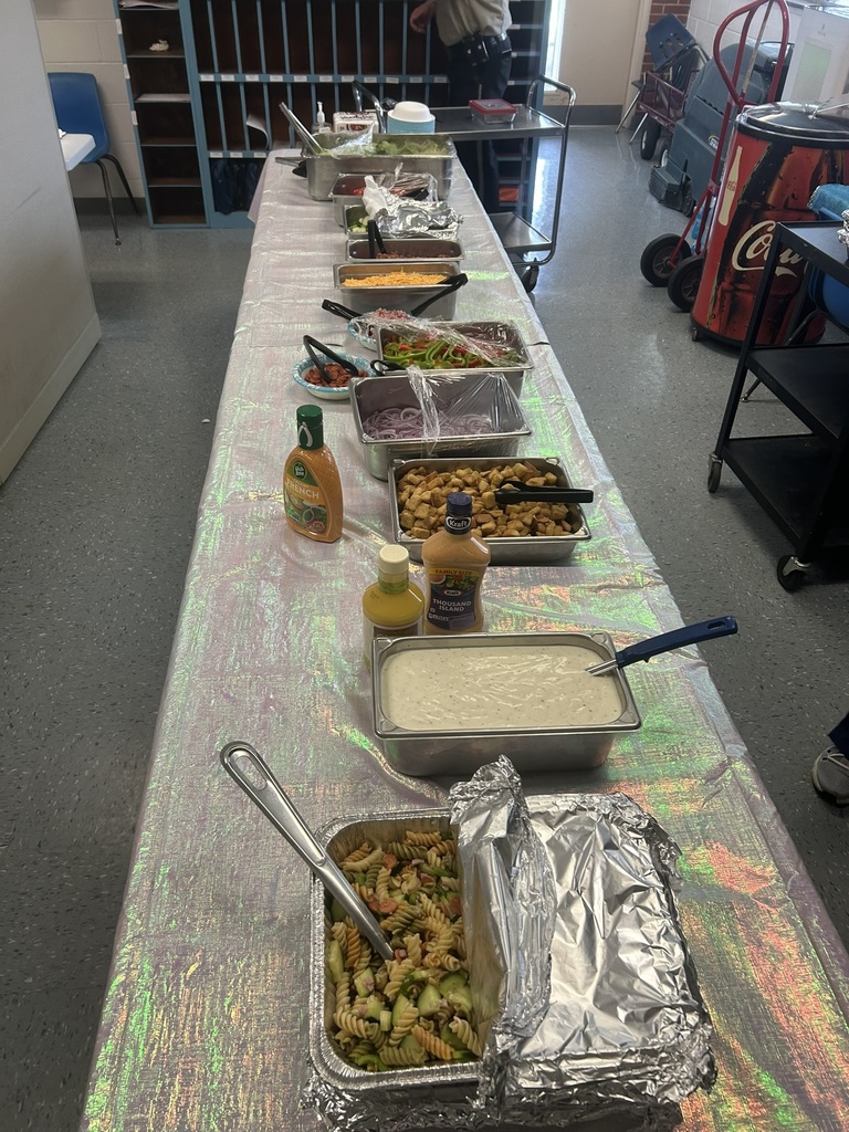 A long table filled with salad bar items, pasta salad, dressings, toppings, and fresh vegetables is prepared for teachers during Teacher Appreciation Week.