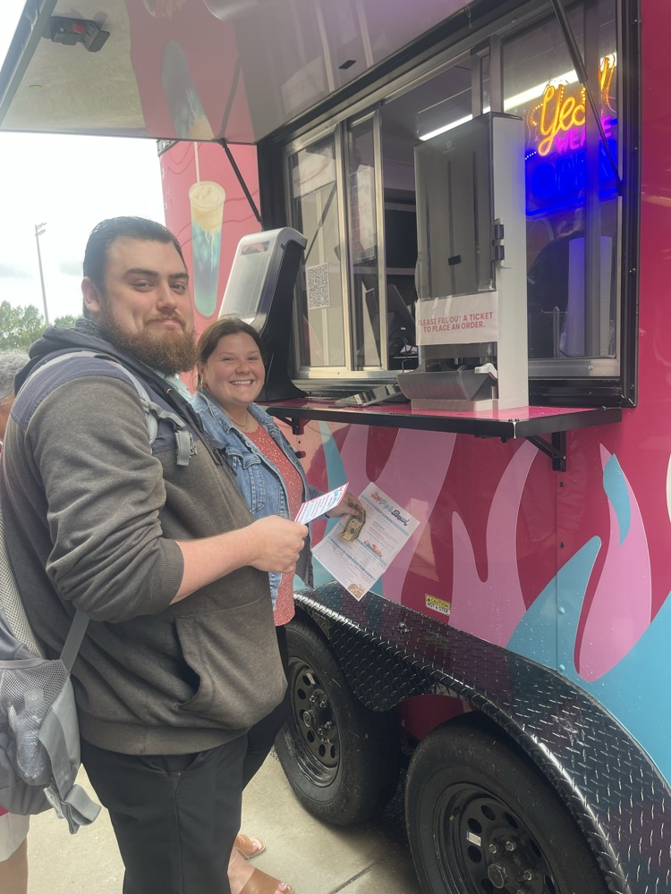 A man with a book bag on standing in line with a woman waiting to order from a food truck