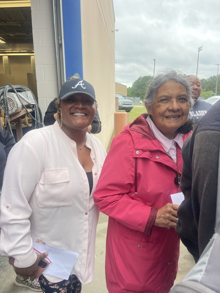 A woman and a white shirt stands beside a lady in a pink jacket as they pose for the camera