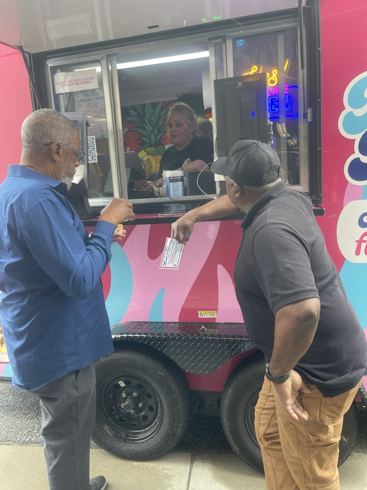 two gentlemen propped up on a food truck waiting for their treats to be prepared