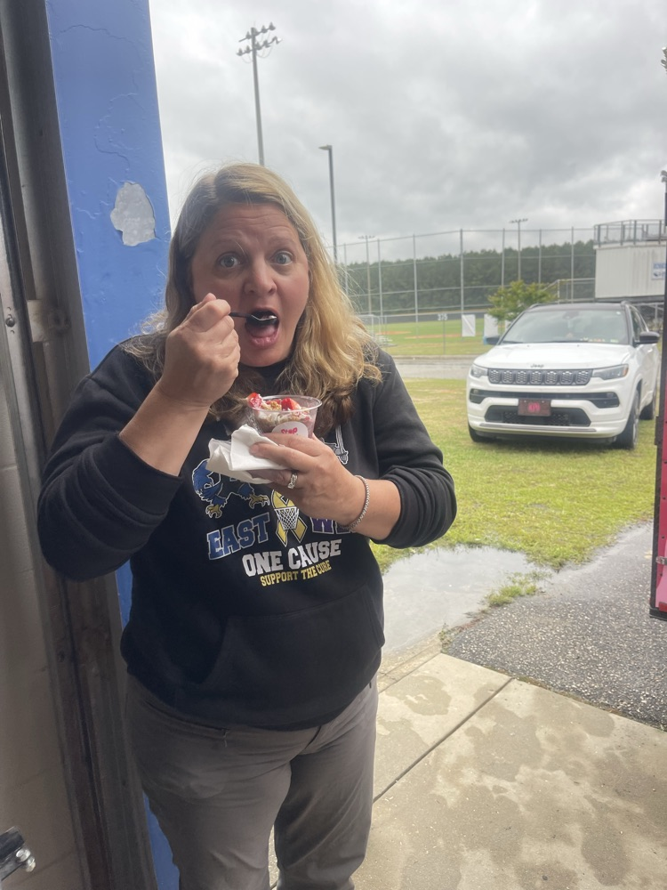 Woman in a black shirt prepares to take a bite of a delicious treat. It is raining in the back of the photo.