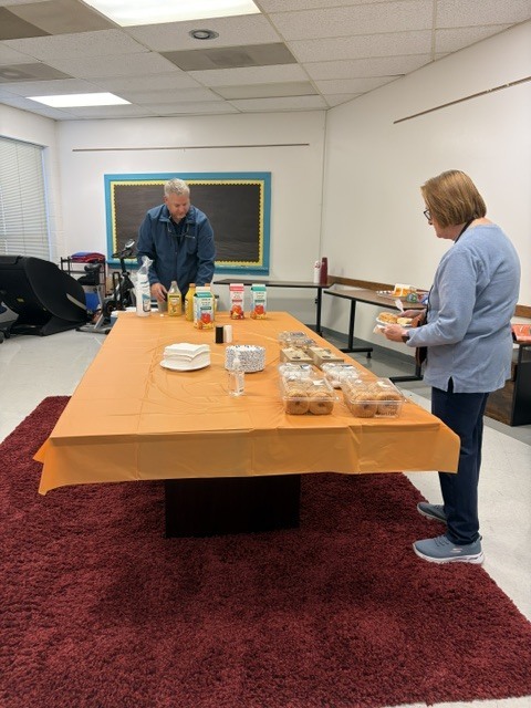 Two community members prepare a breakfast and snack table with pastries, condiments, and drinks for ETMS staff during Teacher Appreciation Week.