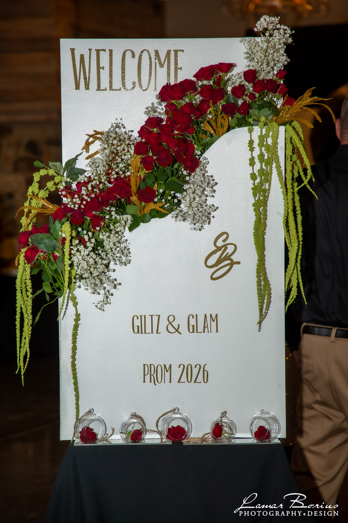 white board with flower arrangement going across it. It says welcome EB Glitz and Glam Prom 2026