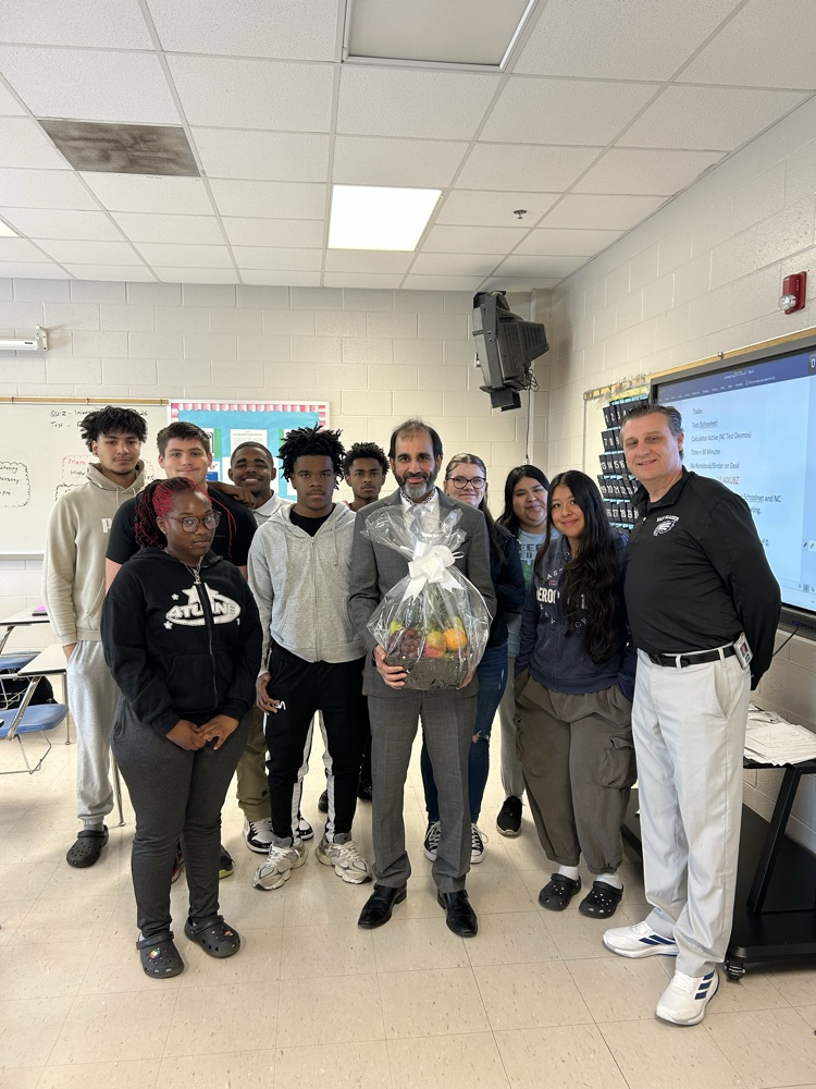 mr. Deswal stands with Dr. Carroll in a group of students as he is presented with a fruit basket