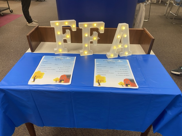 table with blue table cloth, two sheets up paper laying on it, and light up letters that read FFA