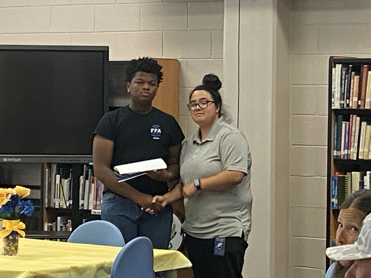 a student in jeans and a black ffa tshirt is presented a certificate by Ms. McMillian in black pants and a grey shirt.