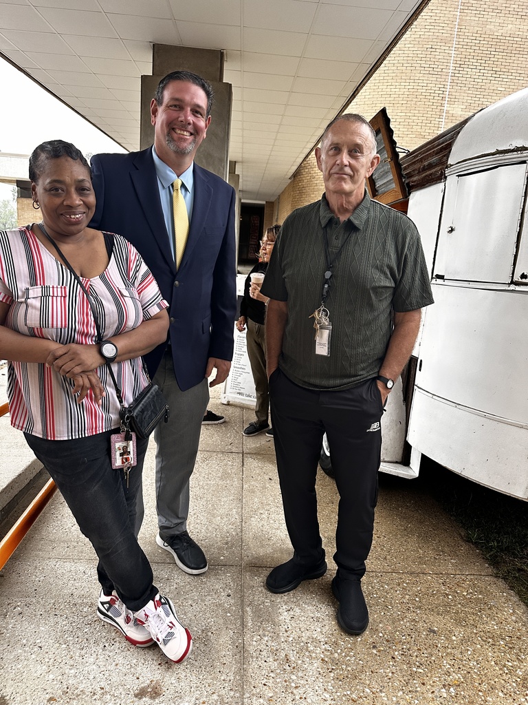 Three staff members pose together outside near the Brew coffee trailer, smiling at the camera.