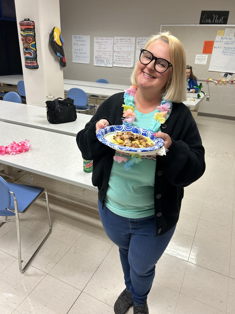A teacher in jeans and a teal shirt shows off her plate of food