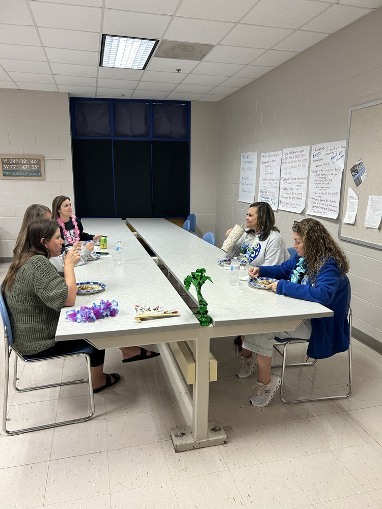 5 teachers gather around a table to enjoy their meal and talk with one another 