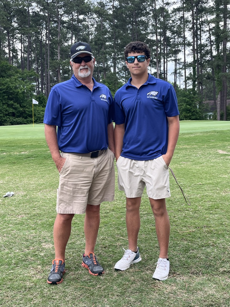 coach Huff and Henry Simmons stand together on the golf course both wearing kaki shorts and Eagle blue polos