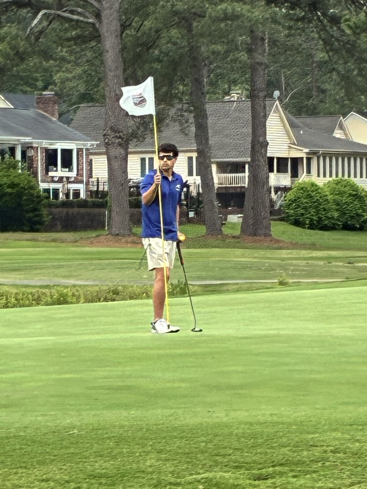 Henry stands holding the flag on the golf course with a gold club in his hand 