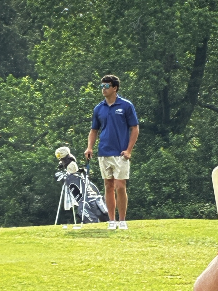 Henry stands holding the flag on the golf course with a gold club in his hand 