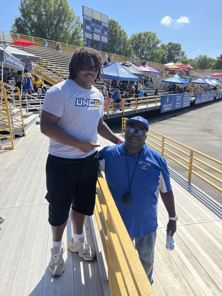 student in black shorts with a white UNCG tshirt shaking hands with a coach in a blue polo