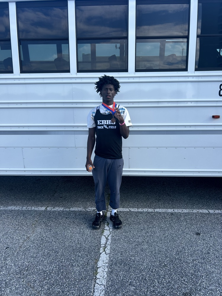 student stands with a medal in front of a white school bus