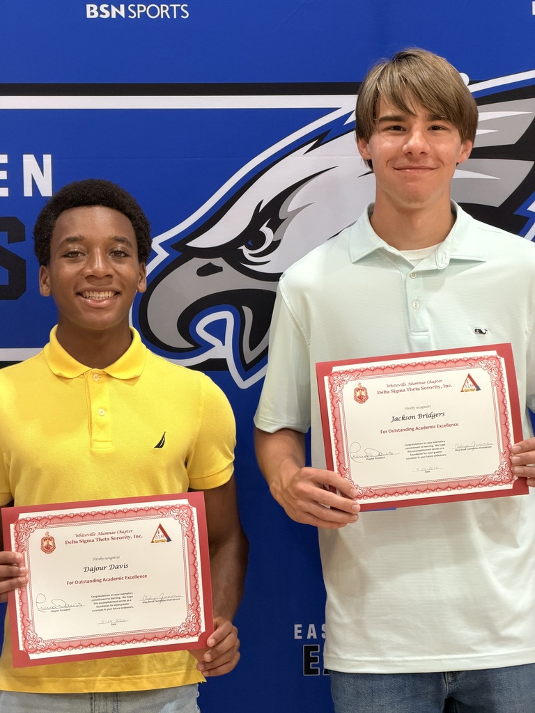 A student in a yellow shirt with a student in a white polo standing in front of the East Bladen backdrop posing with certificate certificates