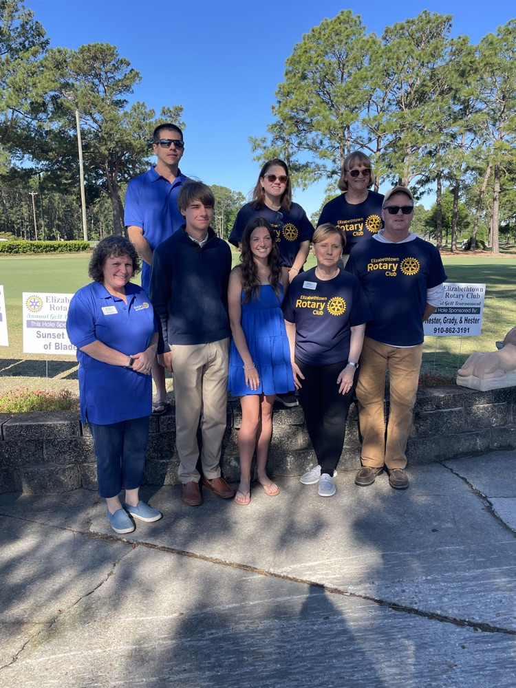 four people from the Rotary club stand with four students that are being recognized as scholarship recipients. They stand in front of a golf course.