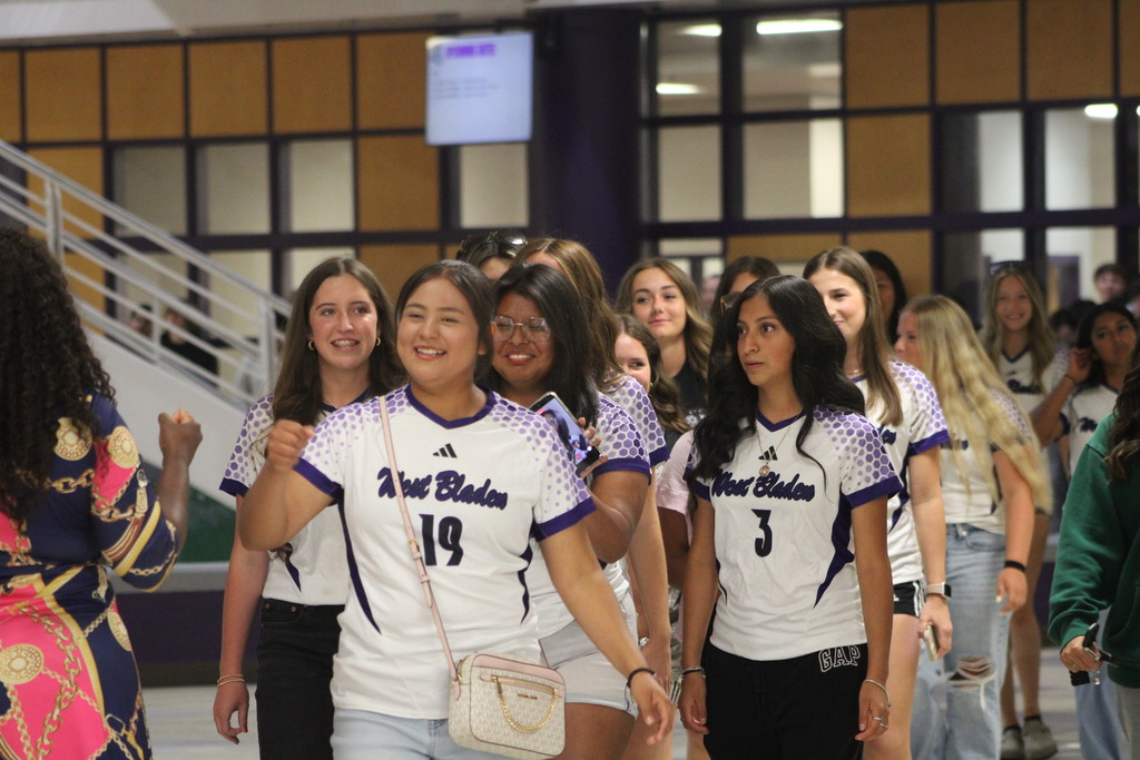West Bladen Lady Knights varsity soccer players walk through the school during their send-off before the Wake Prep match. The team is surrounded by classmates and supporters cheering them on in the atrium.