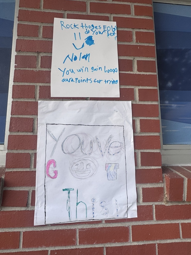 A bright and cheerful student-made poster hangs on a brick wall reading “Test Day You Are READY!” in rainbow-colored letters surrounded by stars, swirls, and encouraging notes for students taking the EOG test.