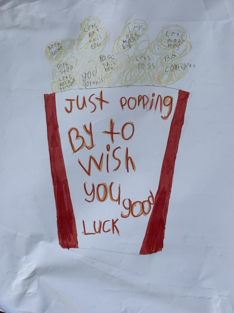 A bright and cheerful student-made poster hangs on a brick wall reading “Test Day You Are READY!” in rainbow-colored letters surrounded by stars, swirls, and encouraging notes for students taking the EOG test.