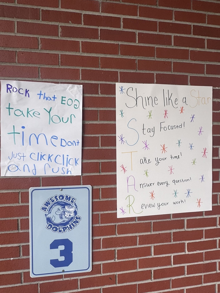 A bright and cheerful student-made poster hangs on a brick wall reading “Test Day You Are READY!” in rainbow-colored letters surrounded by stars, swirls, and encouraging notes for students taking the EOG test.