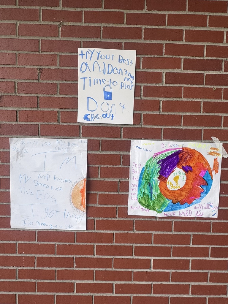 A bright and cheerful student-made poster hangs on a brick wall reading “Test Day You Are READY!” in rainbow-colored letters surrounded by stars, swirls, and encouraging notes for students taking the EOG test.