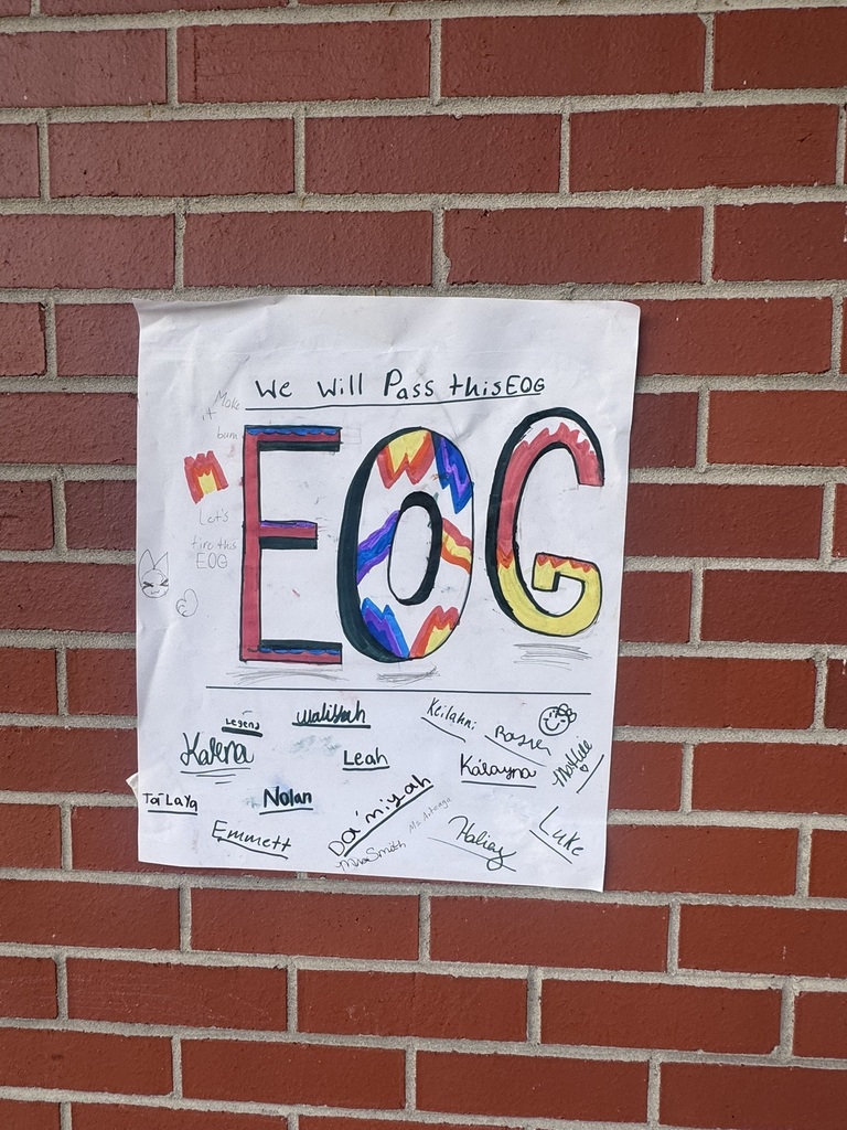 A bright and cheerful student-made poster hangs on a brick wall reading “Test Day You Are READY!” in rainbow-colored letters surrounded by stars, swirls, and encouraging notes for students taking the EOG test.